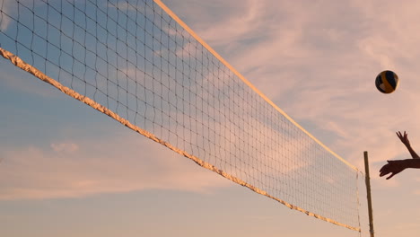 Athletic-girl-playing-beach-volleyball-jumps-in-the-air-and-strikes-the-ball-over-the-net-on-a-beautiful-summer-evening.-Caucasian-woman-score-a-point.